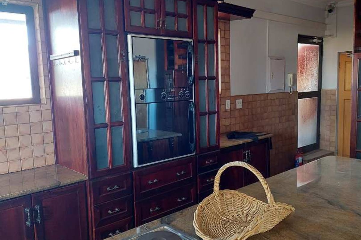 A functional kitchen featuring dark wood cabinetry, granite countertops, a built-in oven, and a central island with an integrated electric hob.