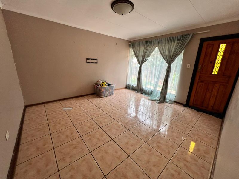 A spacious living room featuring neutral wall tones, tiled flooring, and a solid timber entrance door, offering a blank canvas for interior design.