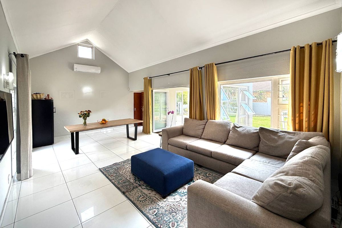 Spacious living area featuring vaulted ceilings, large windows with garden views, tiled flooring, and a wall-mounted air conditioning unit.