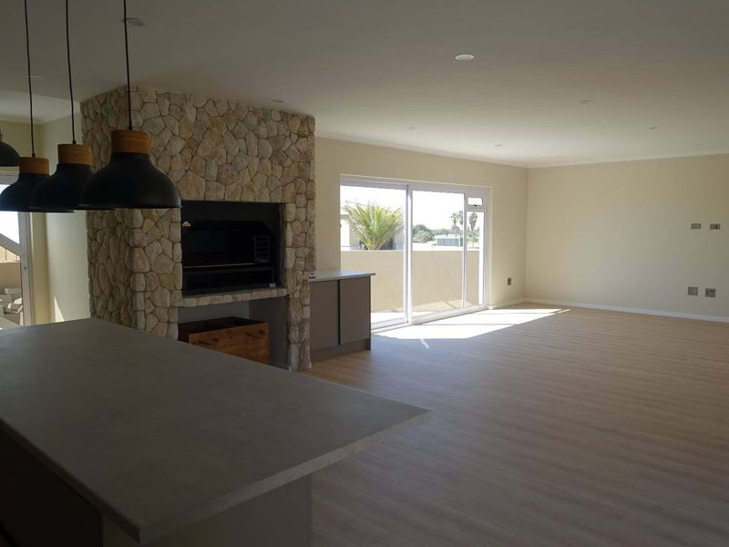 Spacious open-plan living area featuring a striking stone-clad built-in fireplace, modern laminate flooring, and large sliding doors leading to an outdoor space.
