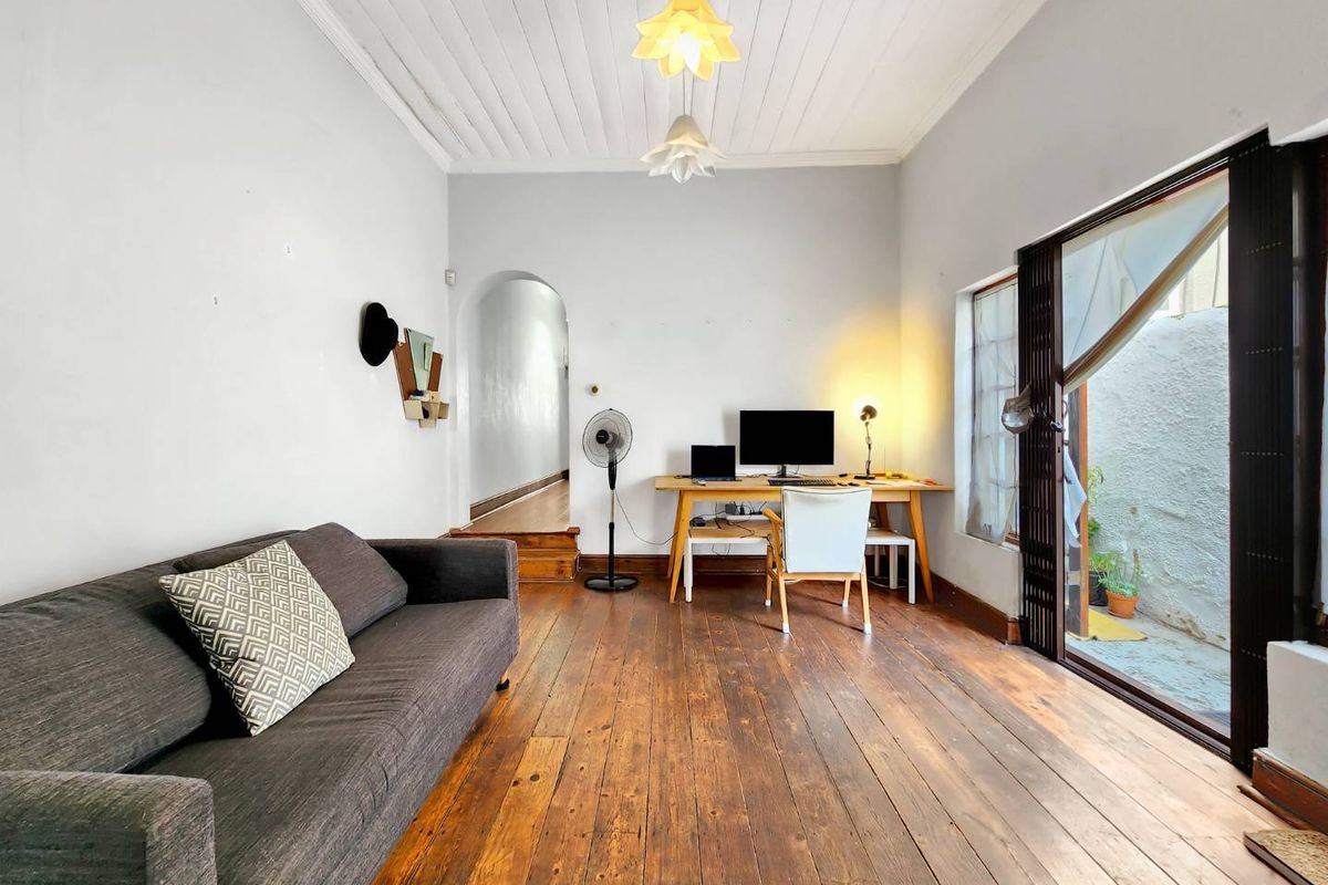 A living room featuring original timber flooring, a tongue and groove ceiling, and an archway leading to a hallway with access to an outdoor area.
