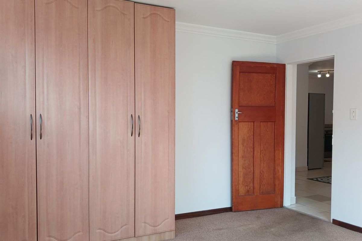 A clean, empty bedroom featuring built-in timber-look wardrobes, neutral walls, carpeted flooring, and a classic wooden door leading to an adjacent space.