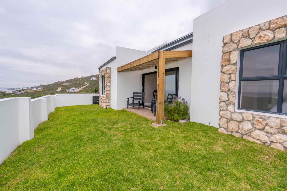 A well-maintained rear garden featuring a covered patio area with timber pergola, stone-clad exterior walls, and expansive lawn space.