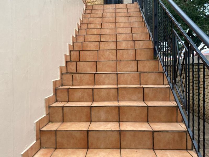 An exterior staircase featuring terracotta-style tiles and a black metal balustrade leading to the property entrance.
