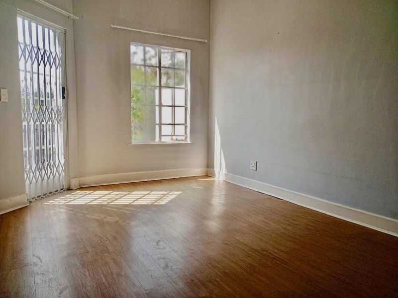 An empty bedroom featuring laminate flooring, a security gate, and a window with burglar bars, offering a blank canvas for personalization.
