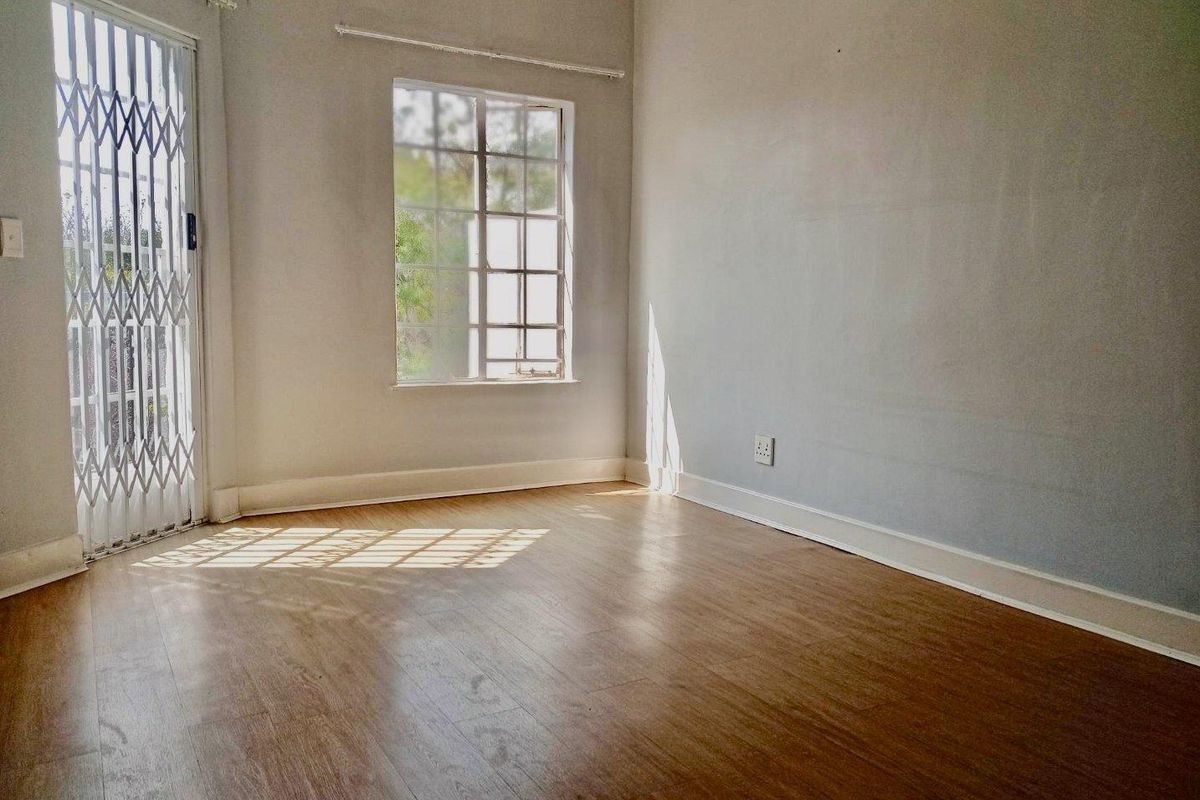 An empty bedroom featuring laminate flooring, a security gate, and a window with burglar bars, offering a blank canvas for personalization.