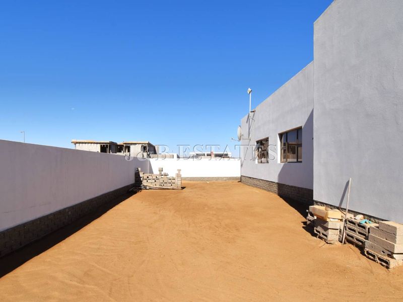 A spacious, undeveloped rear yard area featuring a high boundary wall and plastered exterior wall finish, offering potential for landscaping or outdoor living.