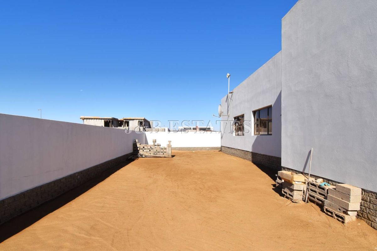 A spacious, undeveloped rear yard area featuring a high boundary wall and plastered exterior wall finish, offering potential for landscaping or outdoor living.