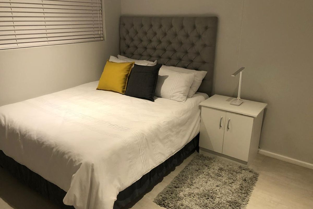 A cozy bedroom featuring neutral wall tones, light-colored flooring, and fitted window blinds.