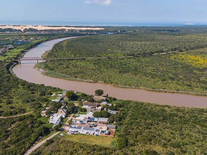 Aerial view of the property situated along a river, showcasing the building layout, roof-mounted solar panels, and surrounding natural landscape.