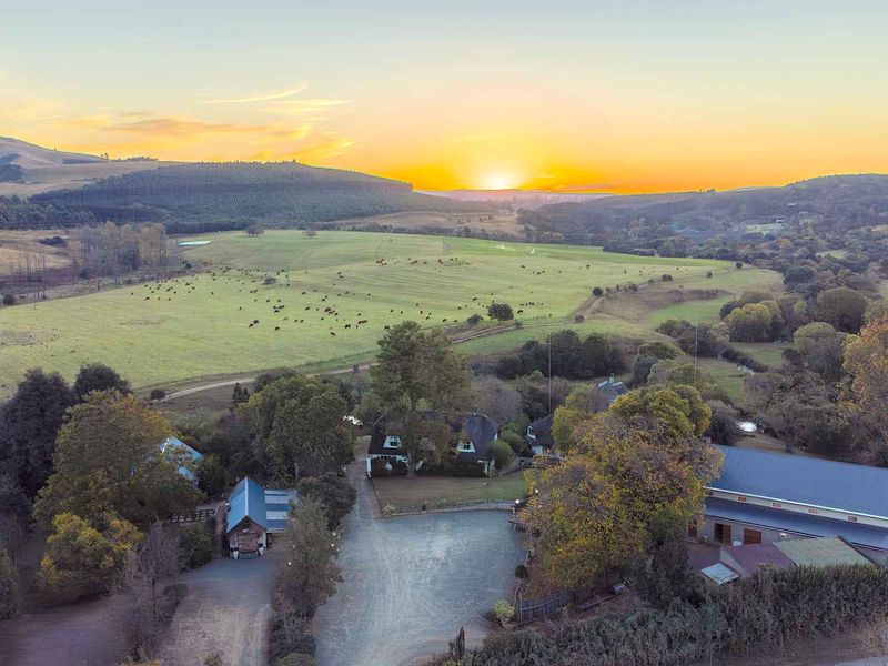 Aerial view of the guest house property featuring multiple buildings, a gravel driveway, and expansive surrounding farmland at sunset.