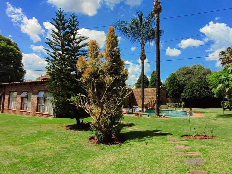 Spacious landscaped garden featuring a well-maintained lawn, mature trees, and a swimming pool area adjacent to the brick-clad house exterior.