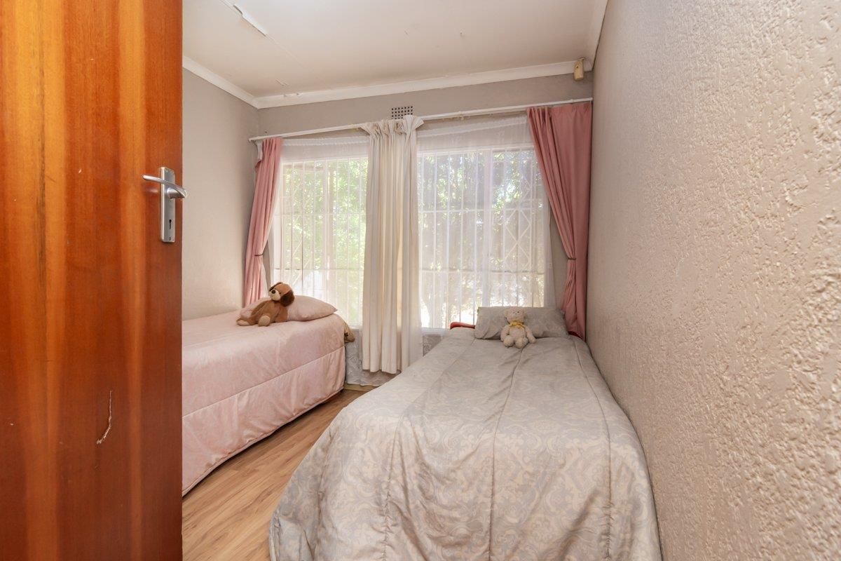 A compact bedroom featuring laminate flooring, large windows with security bars, and textured wall finishes.