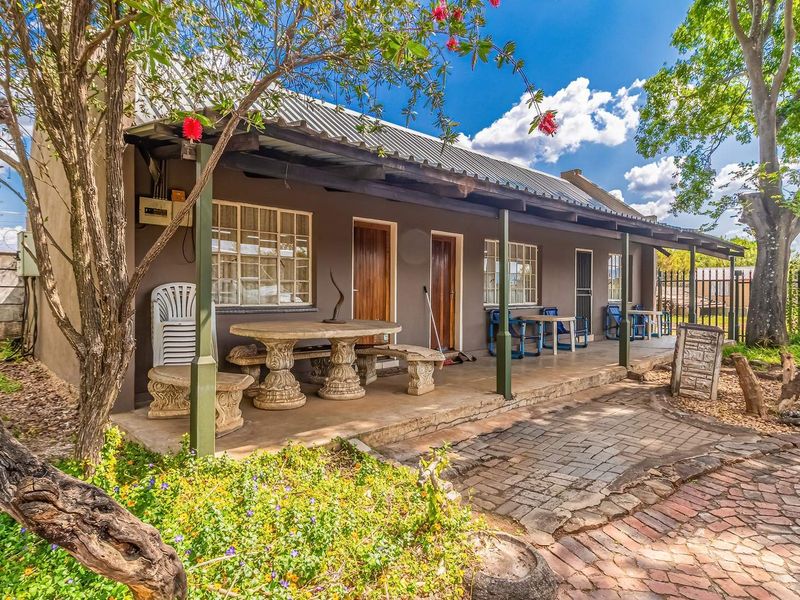 A covered outdoor patio area featuring paved flooring and direct access to the main building, set within a landscaped garden environment.