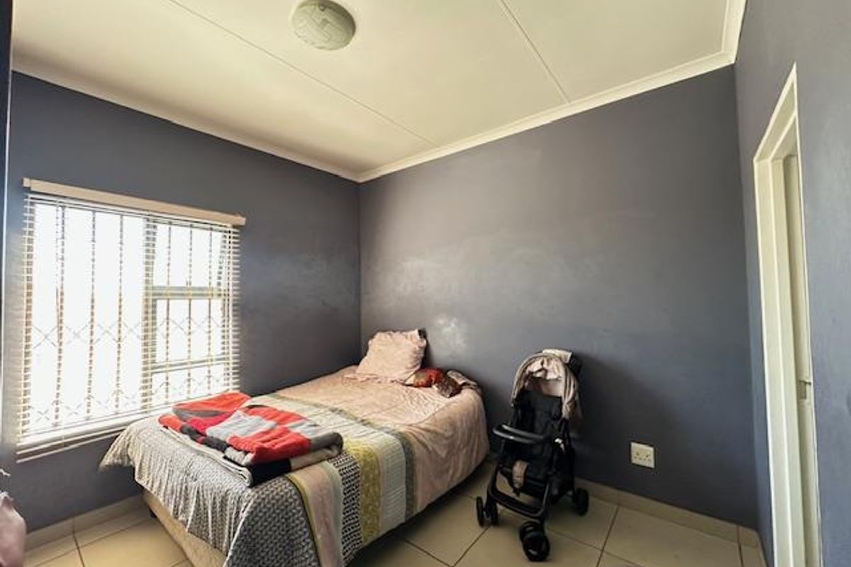 A bedroom featuring tiled flooring, a window with security bars and blinds, and dark-toned walls.