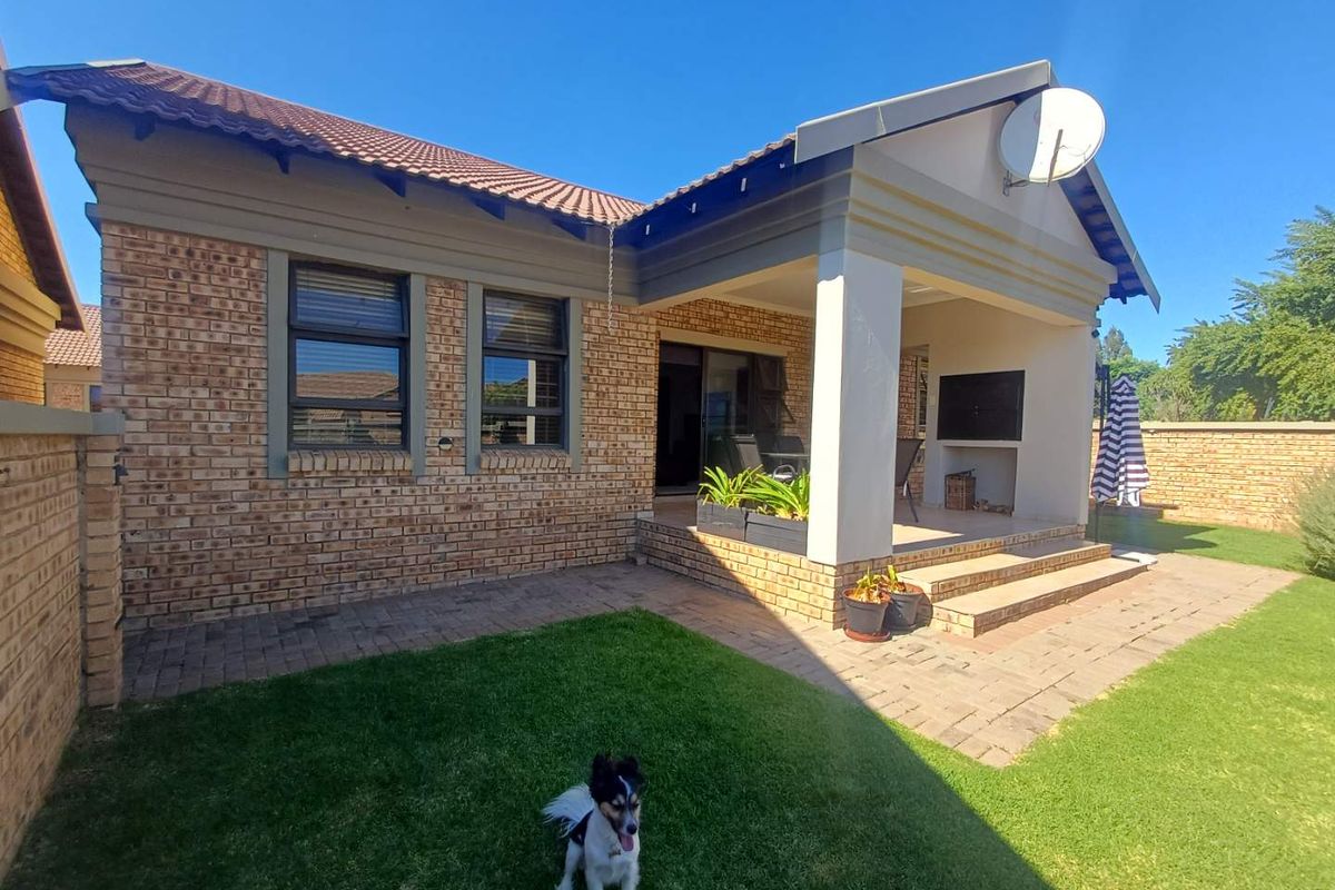 Rear view of the townhouse featuring a covered patio with a built-in braai, brick facade, tiled roof, and a private garden area.
