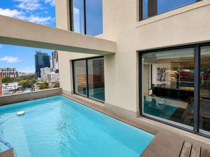 A modern penthouse balcony featuring a private swimming pool with city views and large sliding glass doors leading into the living area.