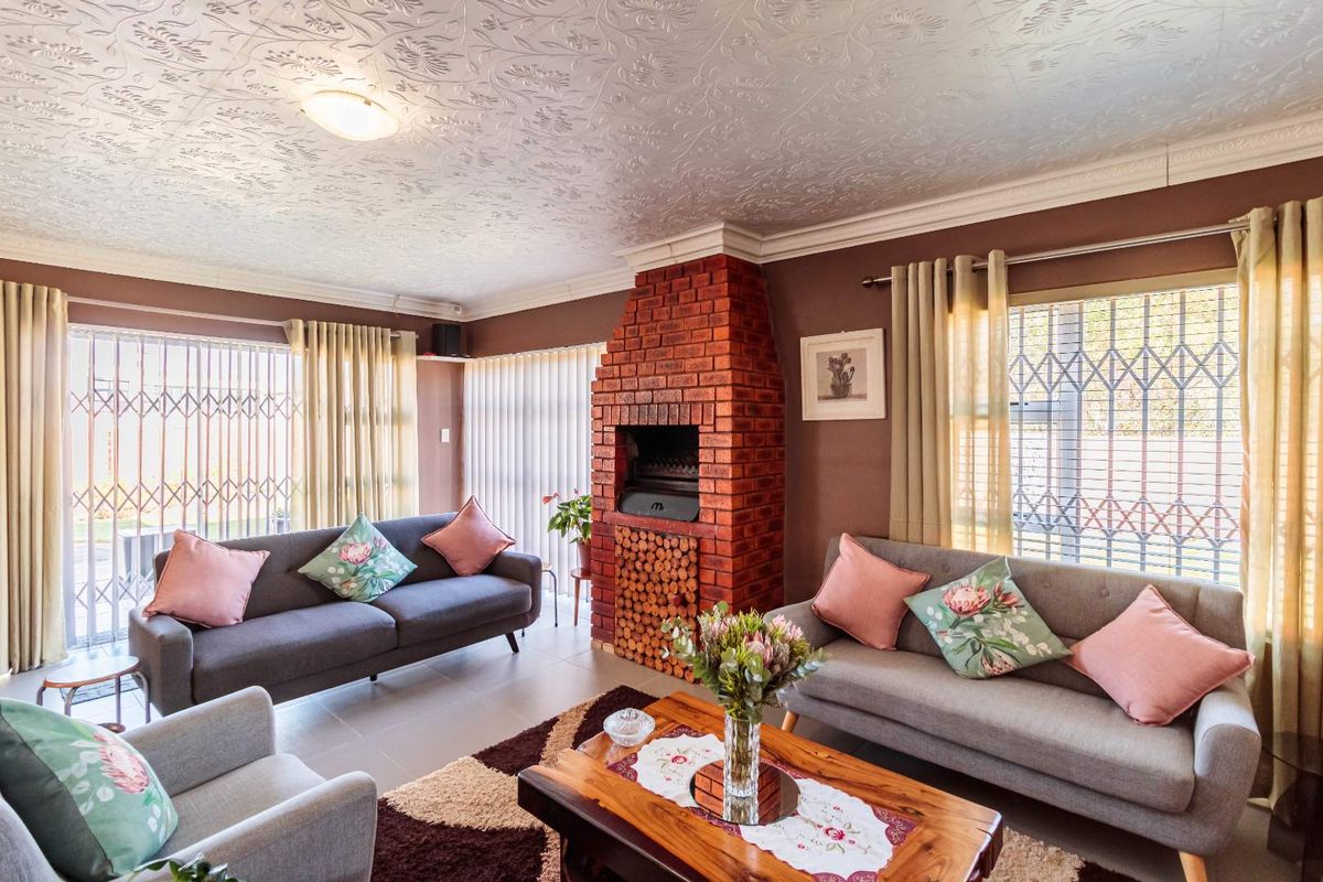 A cozy living room featuring a prominent red brick fireplace with integrated wood storage, tiled flooring, and large windows with security gates.