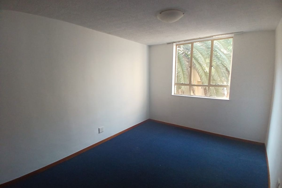 A vacant bedroom featuring blue carpeting, white walls, and a window providing natural light and a view of greenery.