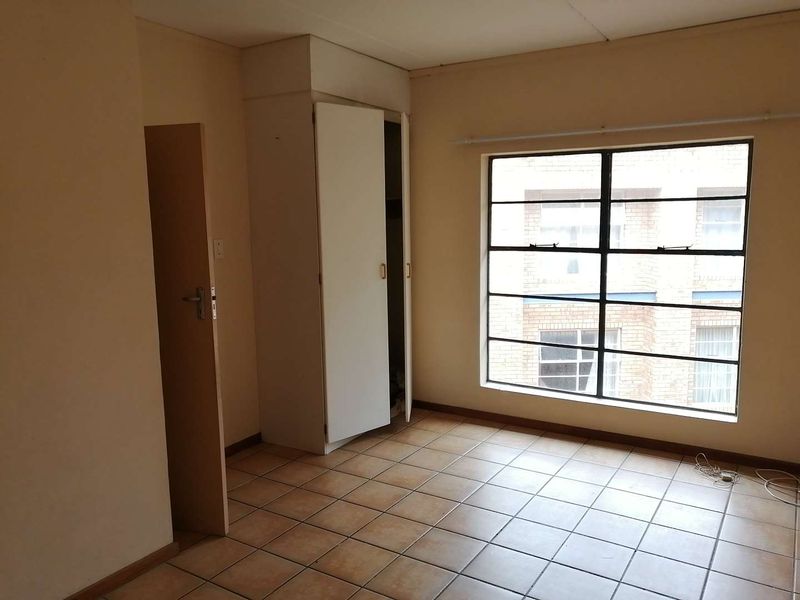 An empty bedroom featuring tiled flooring, a built-in cupboard, and a large steel-framed window providing natural light.