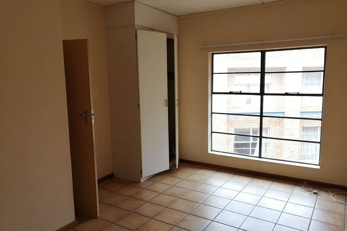 An empty bedroom featuring tiled flooring, a built-in cupboard, and a large steel-framed window providing natural light.
