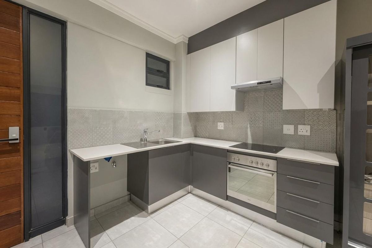 Modern kitchen featuring sleek grey and white cabinetry, stone countertops, integrated oven, electric hob, and a stylish tiled backsplash.