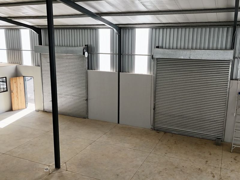 Spacious industrial warehouse unit featuring high ceilings, concrete flooring, and dual roller shutter doors for efficient access.
