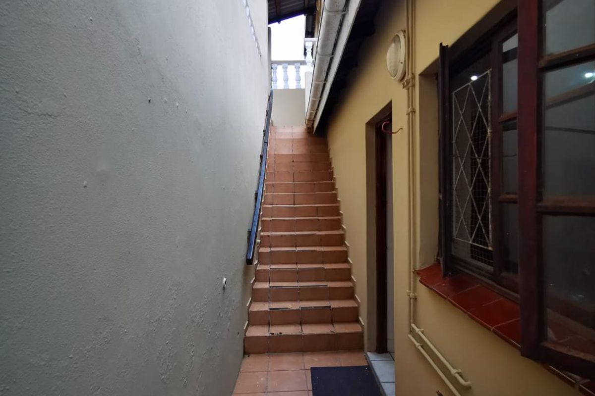 An exterior side passage featuring tiled stairs leading to an upper level, with a wall-mounted outdoor tap and timber-framed window.
