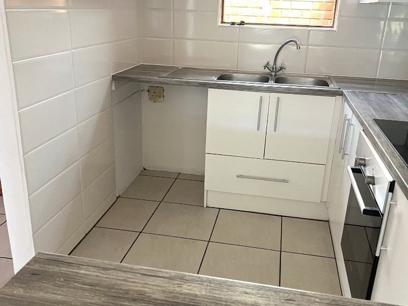 A compact kitchen featuring white cabinetry, laminate countertops, a stainless steel double sink, and a built-in oven with tiled flooring and splashbacks.