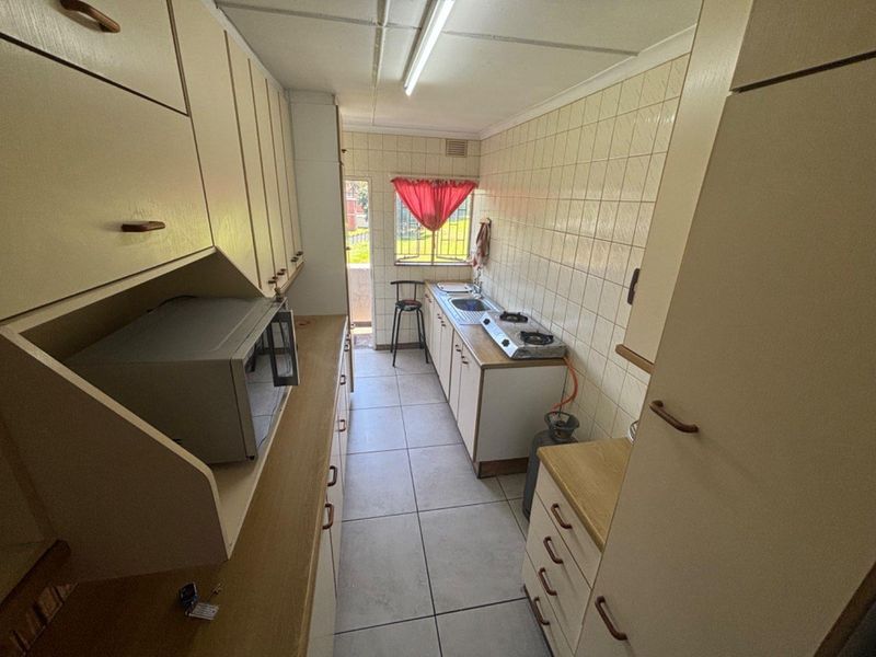 A compact, functional kitchen featuring dated cabinetry, tiled splashbacks, a stainless steel sink, and a gas hob with tiled flooring throughout.