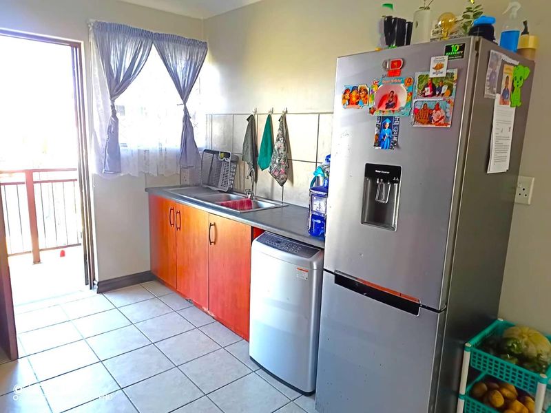 A functional kitchen featuring laminate cabinetry, a stainless steel sink, tiled backsplash, and direct access to an outdoor balcony area.