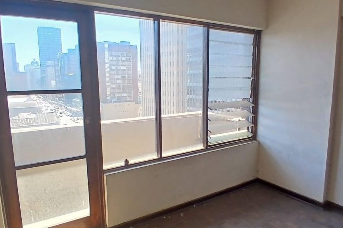 An empty living area featuring large windows with city views, a glass door, and dated finishes, offering a blank canvas for renovation.