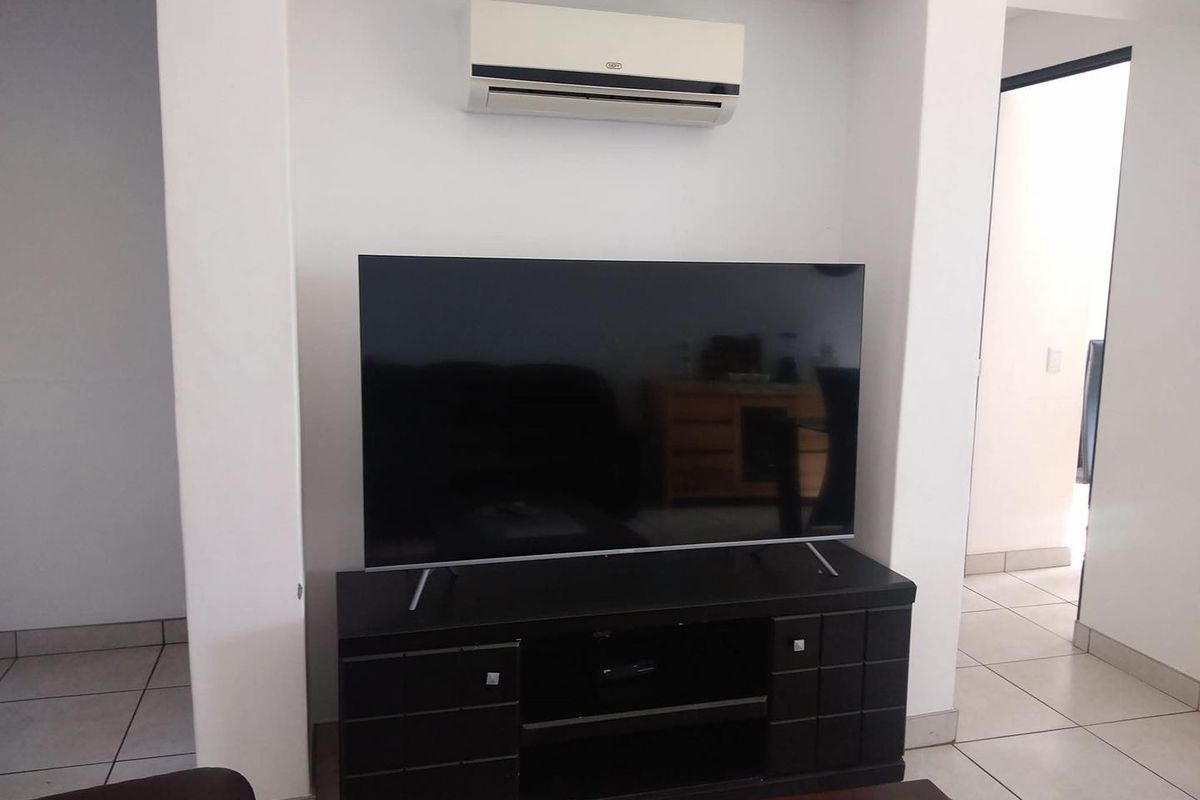 A living room area featuring a recessed wall niche with a wall-mounted air conditioning unit and tiled flooring.