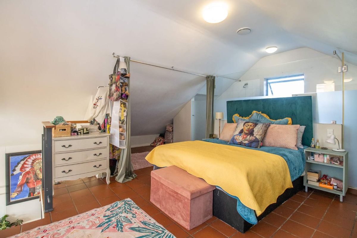 A bedroom located in an attic space with sloped ceilings, tiled flooring, and a window providing natural light.