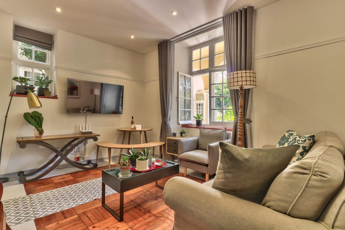 A cozy living room featuring warm timber flooring, recessed ceiling lighting, and large windows that provide natural light and views of the exterior.