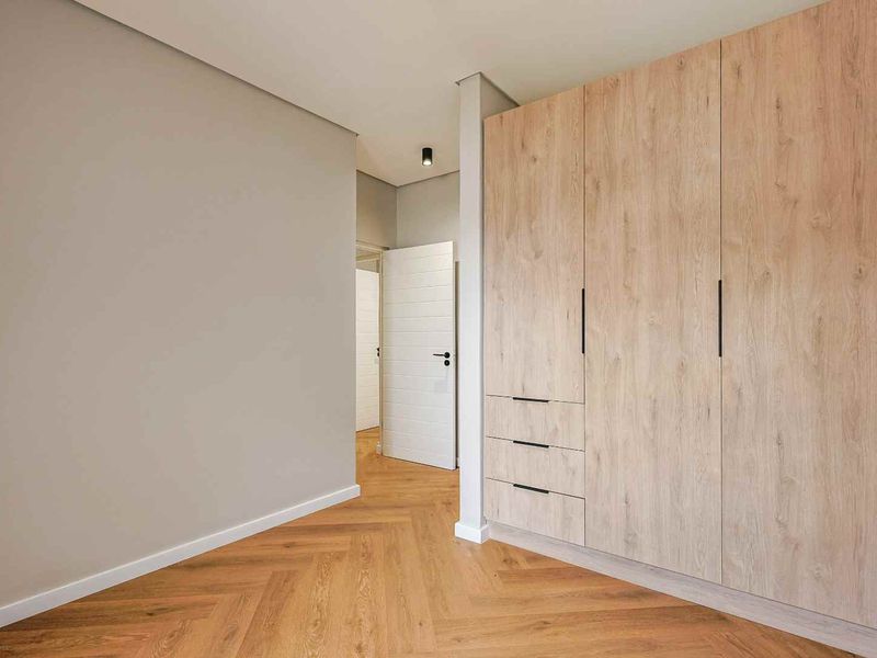 A bright, modern bedroom featuring high-quality herringbone timber flooring and extensive built-in light wood cabinetry with integrated storage.