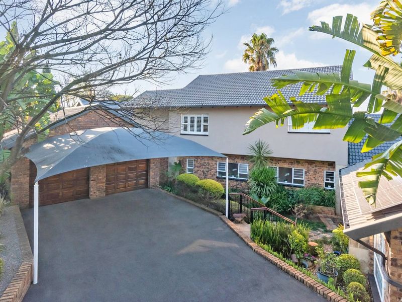 Front view of a two-story brick house featuring a double garage, a shade sail carport, and a well-maintained driveway with established garden beds.