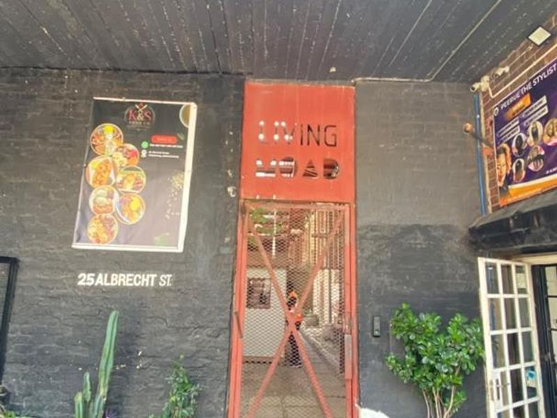 Front entrance of the apartment building featuring a metal security gate, brick paving, and a covered entryway with signage.