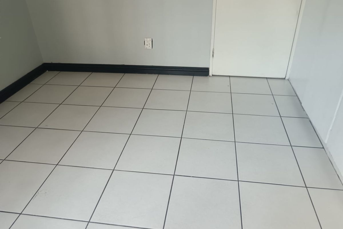 A simple, empty room featuring neutral grey walls, dark contrasting skirting boards, and light-colored ceramic floor tiles.