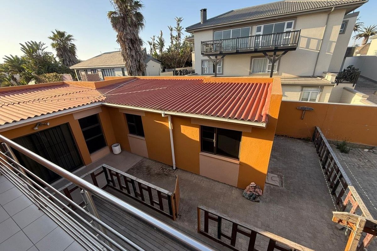 Rear exterior view showing a paved courtyard area, corrugated metal roofing, and boundary walls, captured from an elevated balcony perspective.