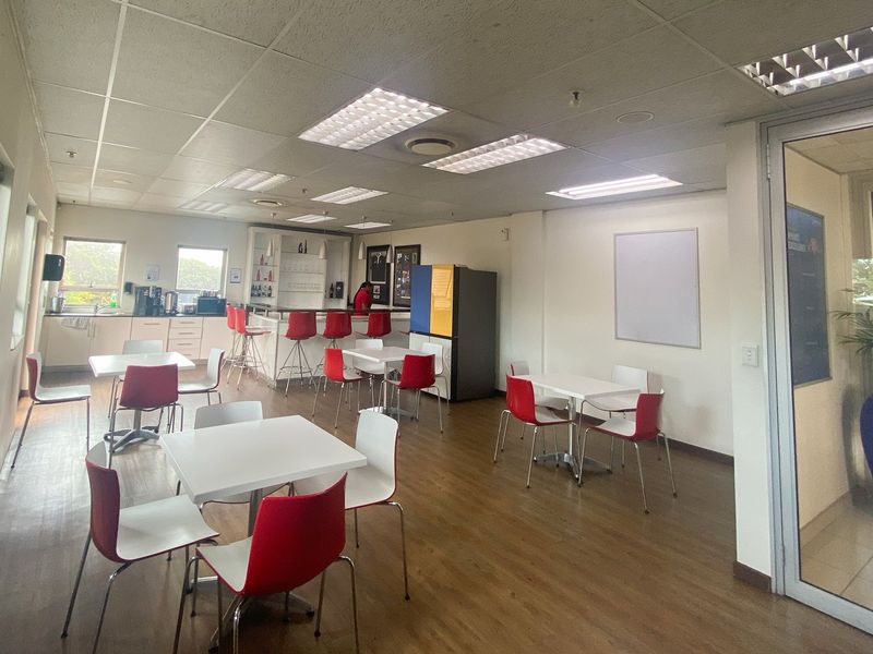 Open-plan industrial office break area featuring a built-in bar counter, suspended ceiling with recessed lighting, and durable laminate flooring.