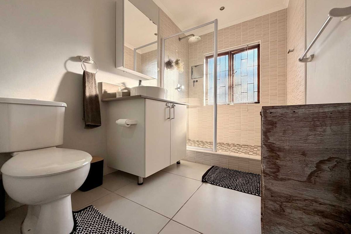A modern bathroom featuring a walk-in shower with glass enclosure, vanity cabinet with basin, and neutral wall tiling.