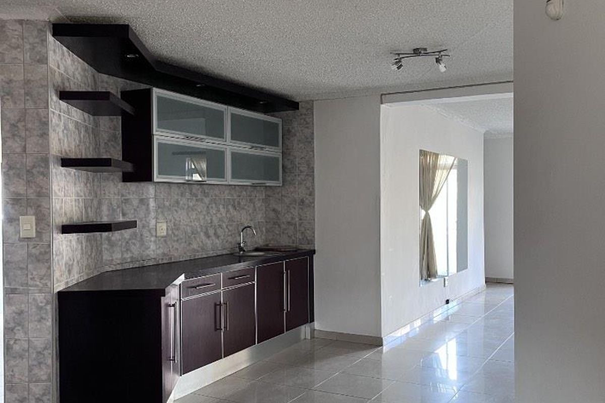 A functional kitchen area featuring dark cabinetry, tiled backsplash, and light-colored floor tiles, flowing into an open-plan living space.