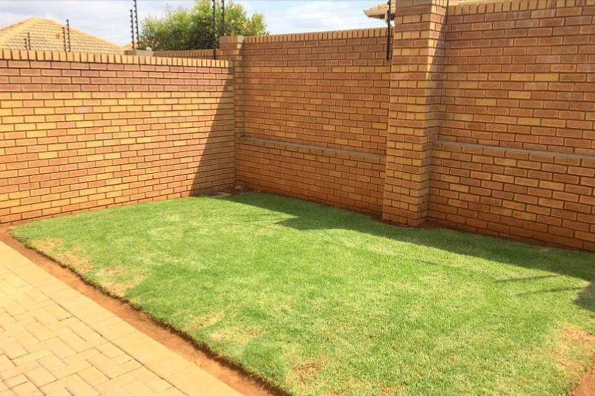 A private rear garden area featuring a well-maintained lawn, paved walkway, and secure brick boundary walls with electric fencing.