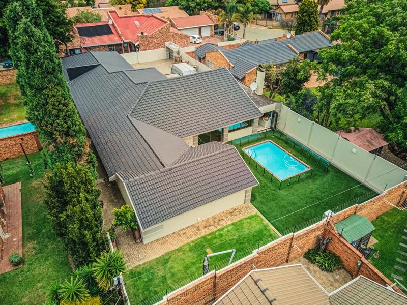 Aerial view of a residential property featuring a tiled roof, private swimming pool, landscaped garden, and secure perimeter walling with electric fencing.