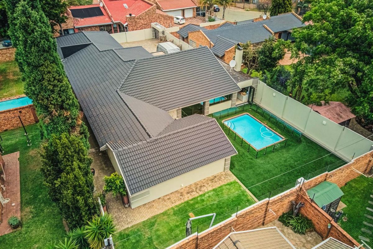 Aerial view of a residential property featuring a tiled roof, private swimming pool, landscaped garden, and secure perimeter walling with electric fencing.