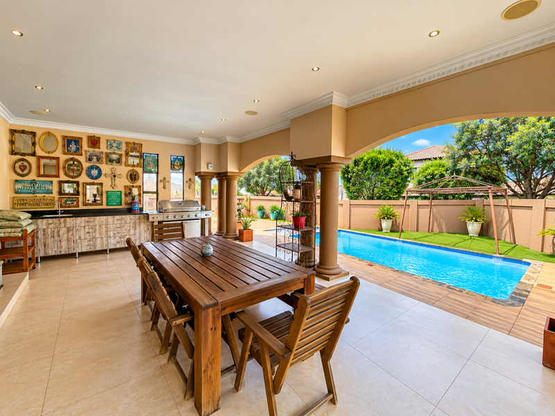 Spacious covered patio featuring built-in cabinetry, a gas grill, and direct access to a private swimming pool and landscaped garden area.