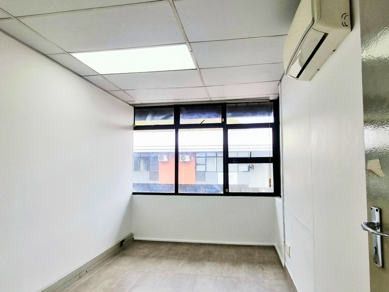 A clean, empty office space featuring a suspended ceiling, recessed lighting, vinyl flooring, and a wall-mounted split-system air conditioning unit.