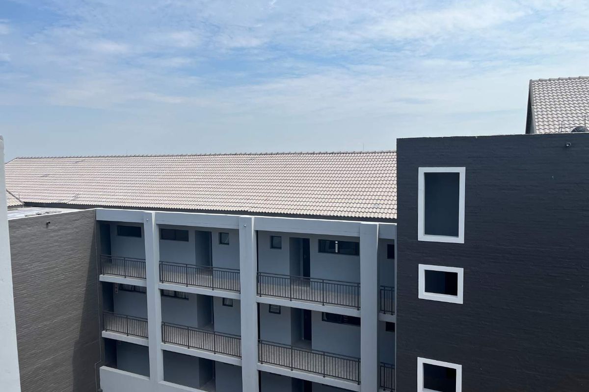Exterior view of a modern apartment complex featuring multi-level balconies with metal railings and a tiled roof structure.