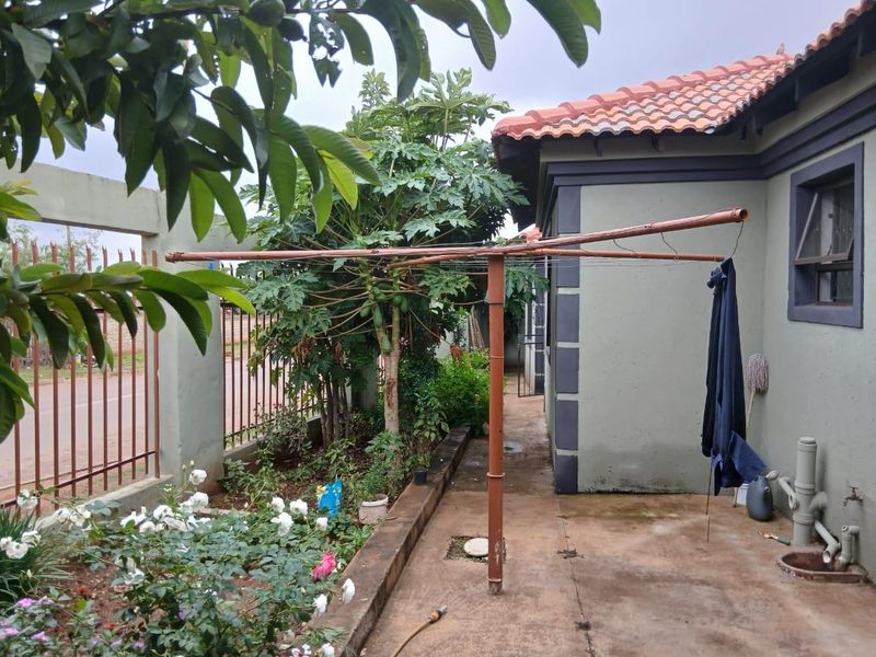 A side exterior area featuring a paved walkway, perimeter wall with metal fencing, and a fixed rotary washing line.